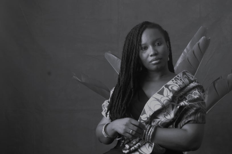 Portrait of Juachi Obi, a woman, seated and wearing her hair down with a pattern shawl draped over her shoulder and gold coloured bangles on both arms